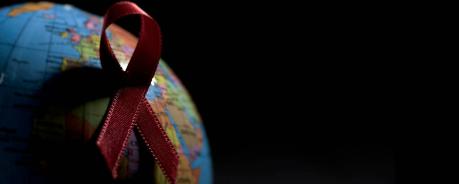 Rote Ansteckschleife auf einem Globus mit viel Schatten vor schwarzem Hintergrund.