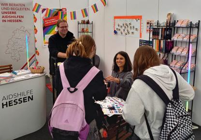 An einer Button-Maschine konnten Besucher*innen eigene Buttons zu queeren Themen getalten. Besucher*innen erhalten am Stand der Aids-Hilfe Buttons.