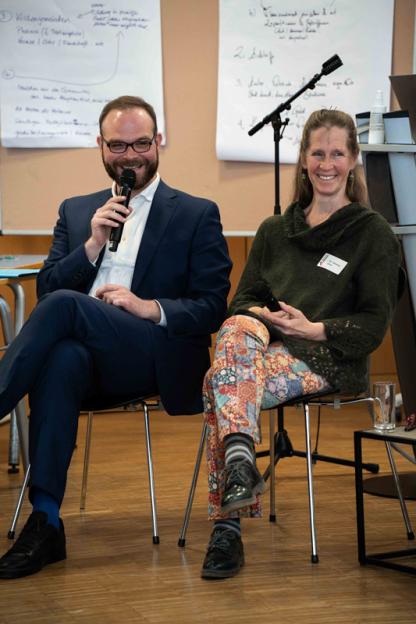 Zwei Personen lächeln während einer Podiumsdiskussion.