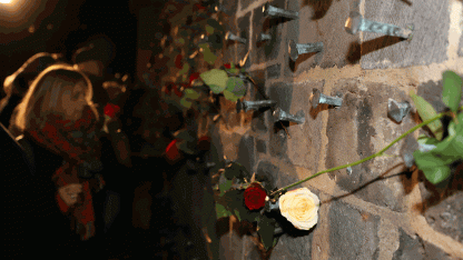 Das Bild zeigt eine Situation bei der Gedenkveranstaltung zum Welt-Aids-Tag 2017 in Frankfurt. Am Gedenkplatz "Verletzte Liebe" an der Peterskirche werden Rosen an die in die Wand in Erinnerung an die Toten eingeschlagenen Nägel angebracht.